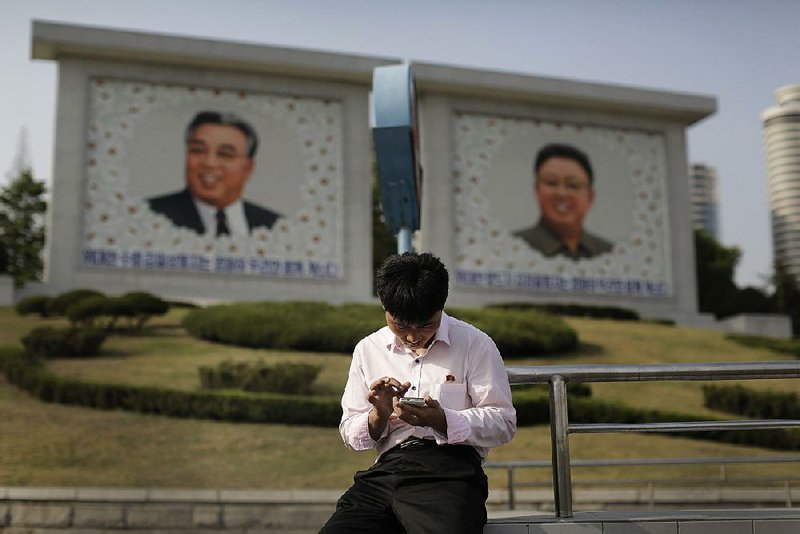 A man sits in front of portraits of the late North Korean leaders Kim Il Sung, left, and Kim Jong Il, right, as he uses his smartphone in Pyongyang, North Korea last week. North Korean officials have unveiled a mobile-friendly online shopping site. 