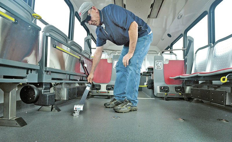 NWA Democrat-Gazette/BEN GOFF Joel Gardner, executive director of Ozark Regional Transit, demonstrates the setup of one of the quick-release wheelchair tie downs in an ARBOC Spirit of Liberty bus Sunday at the Ozark Regional Transit headquarters in Springdale. The modern bus design is larger than many of the ones currently in the Ozark Regional Transit fleet, with an occupancy of 52 and the option to flip up seats to accommodate up to six wheelchairs. A fold-out ramp with a 1,000-pound capacity, combined with kneeling suspension, would make getting on easy for passengers. For photo galleries, go to nwadg.com/photos.