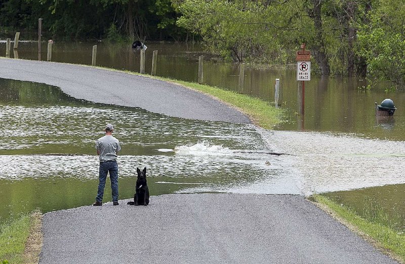 Brandon Harris, with his dog Shadow, watches fish try to swim against the current flowing over Blue Heron Parkway leading into Willow Beach Park in Scott on Wednesday. The recreation area was closed because of the high water from the Arkansas River. 