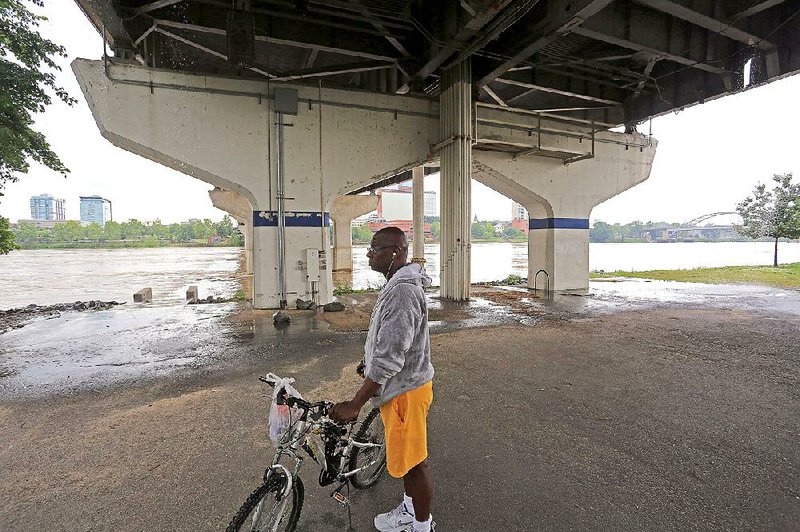 Herb Barner of Little Rock watches the swollen Arkansas River flow as he takes shelter from the rain under the Main Street Bridge in North Little Rock on Thursday. 