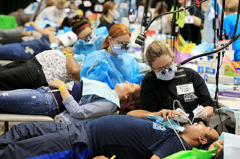 Dental hygienists (from left) Nicole Young, Chelsea Lasey and Laura Andriotis clean patients’ teeth during Friday’s Arkansas Mission of Mercy dental clinic at the Statehouse Convention Center in Little Rock. About 1,000 people showed up for the free care. The clinic continues today. 