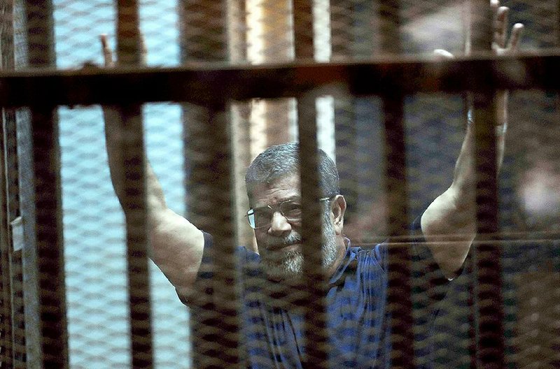 Ousted Egyptian President Mohammed Morsi sits behind a glass partition Saturday in a courtroom in an eastern Cairo suburb. After Saturday’s verdict, he smiled and raised the four-finger signal that his supporters waved during sit-ins.
