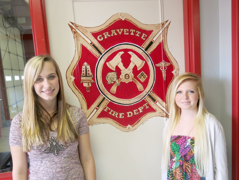 Photo by Susan Holland Destiny Butterworth, a senior at Gravette High School, and Rebecca Gordon, a junior, pose beside the new logo they recently painted in the entryway of the Gravette fire station. Destiny and Rebecca are students in Mollie Hendrick&#8217;s Art II class. It took them about a month to complete the painting. Fire chief Rob Douthit sketched an idea of what he wanted and Art II students designed the logo.
