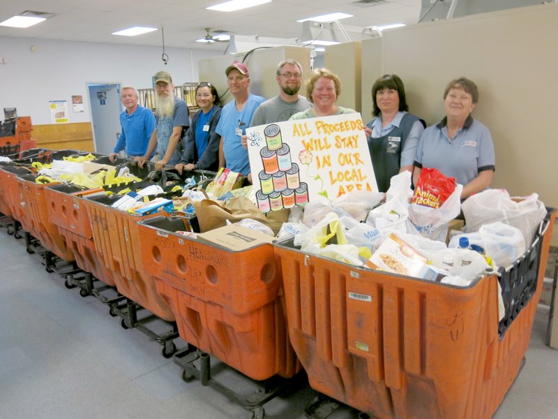 Photo by Susan Holland Gravette postmaster Gerald Garner, left, local mail carriers Roy Ford, Anita Young, Danny Boling, Paul Martin and Michelle Howard and mail clerks Lorrie Amos and Karen Wilkins pose with several of the bins of food collected in this year&#8217;s Stamp Out Hunger Food Drive. Gravette postal carriers and staff collected 2,342 pounds of food to be donated to local food pantries.
