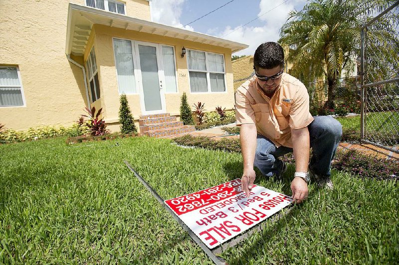 Robert Almirall, director of marketing and special assets coordinator for Mederos & Associates Real Estate Inc., prepares to put up a sign in front of a home in the Shenandoah neighborhood of Miami in late April. 
