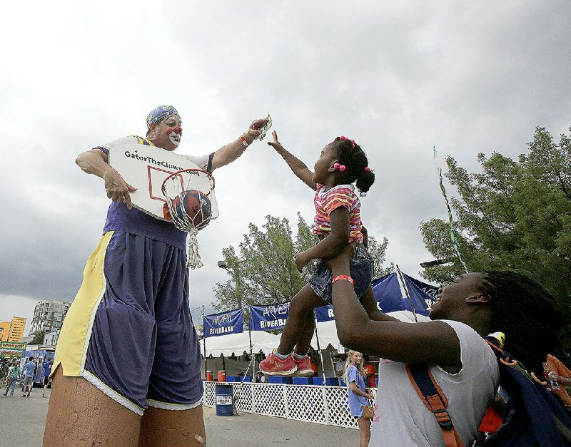 Destiny Goubourn, 3, gets a lift from her sister, Imani Baldwin, 12, so she can reach a prize held by Kenneth Jones, dressed as Gator the Clown, after Destiny made a basket Sunday afternoon at Riverfest in Little Rock. 