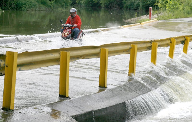 NWA Democrat-Gazette/DAVID GOTTSCHALK A motorist on a scooter passes Tuesday over a flooded low water bridge on Roosevelt Street in Johnson. Heavy rain Monday night pushed Clear Creek out of its banks. For photo galleries, go to nwadg.com/photos.