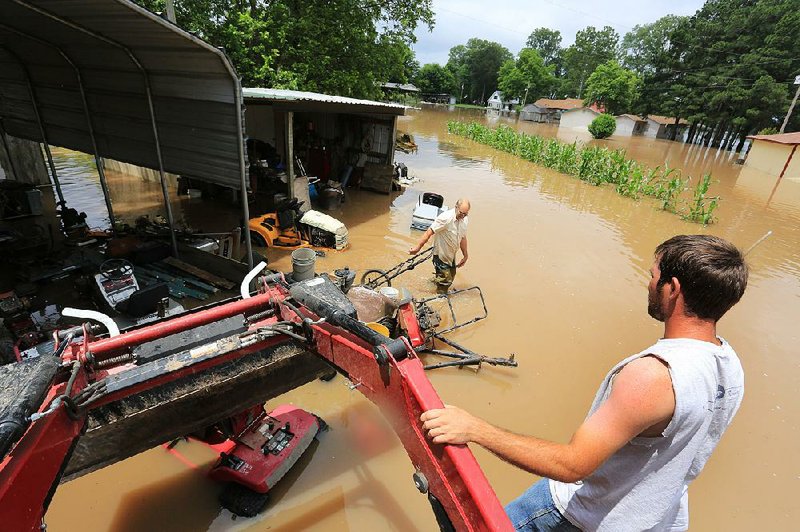 Brandon McCall waits atop his tractor to help load a riding lawn mower into the tractor’s front-end bucket in an area of Wright inundated by floodwaters from the Arkansas River. 