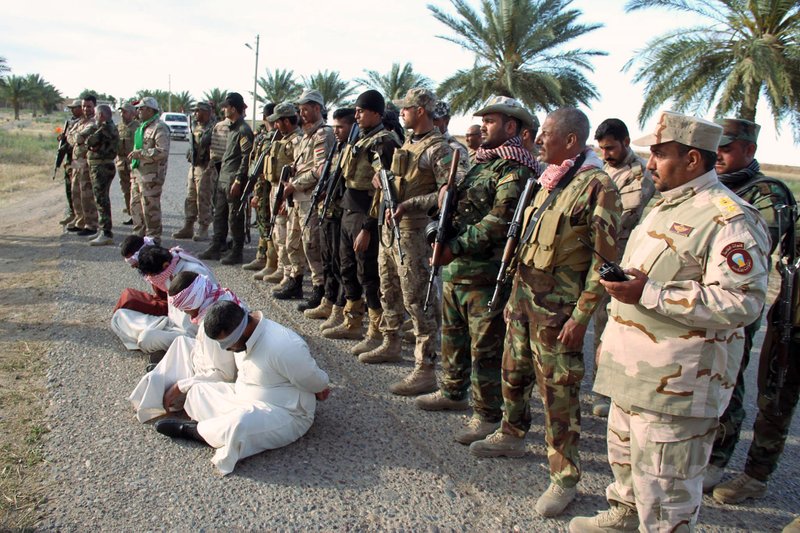 In this image taken Thursday, May 28, 2015, Iraq's Badr Brigades Shiite militia detain four men that they suspect of militants of the Islamic State group outside the oil refinery in Beiji, some 155 miles (250 kilometers) north of Baghdad, Iraq. The men were planning to attack oil refinery checkpoints, the militia said. 
