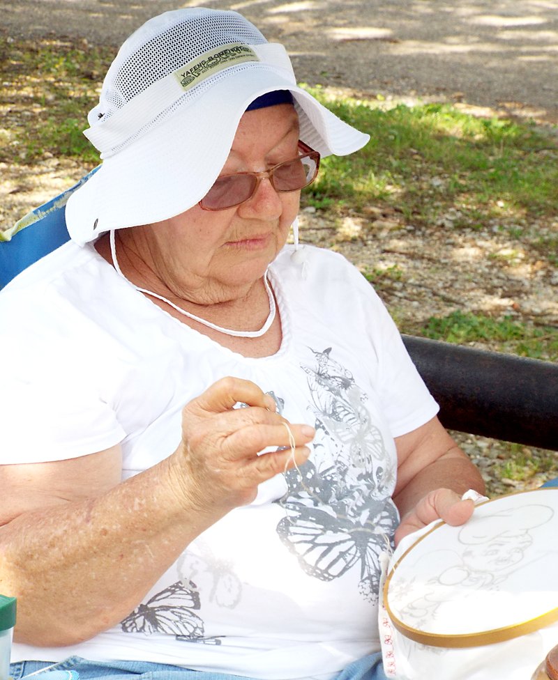 Photo by Randy Moll Doing needlework in the park, Mary Sisson offered hand-stitched tea towels to those attending Old Settlers&#8217; Day in Colcord on Saturday.