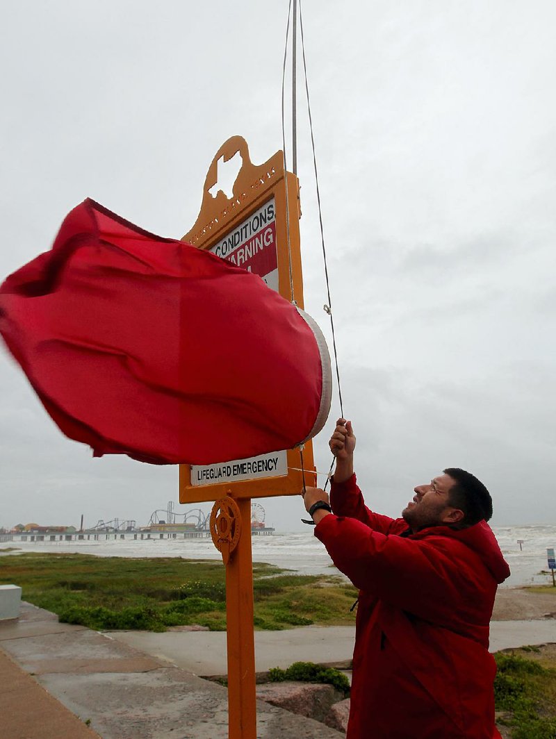 A lifeguard from the Galveston Island Beach Patrol raises red flags Tuesday along the beach seawall to warn people to stay out of the storm-churned surf off Texas.