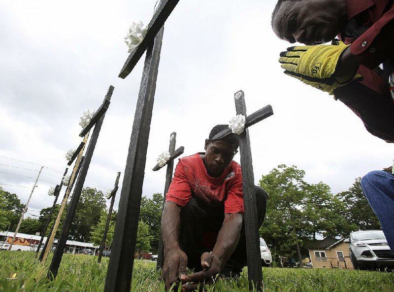 Edjuan Johnson (left) lights a candle Friday in front of one of nine crosses placed by Stop the Violence members at the corner of Martin Luther King Jr. and Daisy L. Gatson Bates drives in Little Rock while Earnest Franklin says a prayer in memory of those killed in a shooting at the Emanuel African Methodist Episcopal Church in Charleston, S.C. 