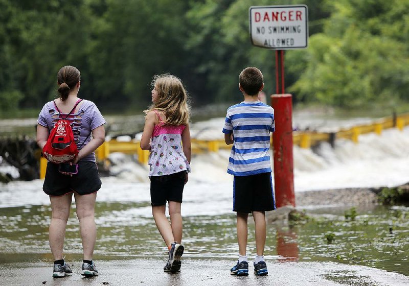 Ksenia Caillouet and her daughter Rayla, 10, and son Rylan, 12, watch the water pour over a low-water bridge Friday on Ball Street in Johnson, where they often walk the trail after rainstorms. 