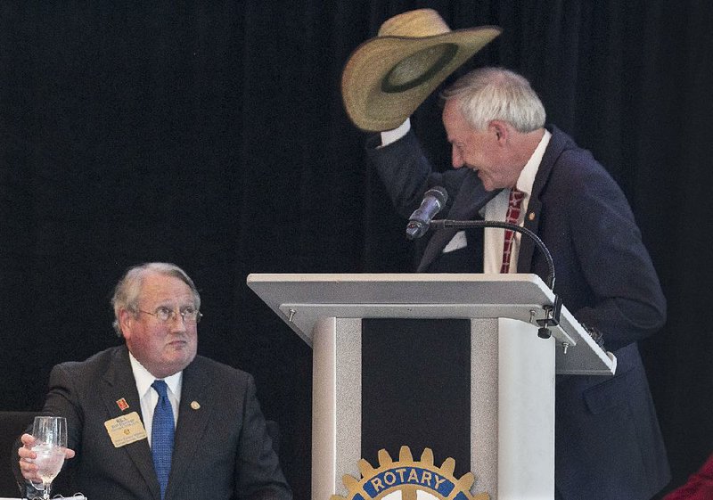 Gov. Asa Hutchinson tips a cowboy hat Tuesday belonging to Little Rock Rotary Club President Bill Booker (left). Booker, who sang a Broadway tune prior to turning the podium over to the governor, had used the hat as a prop. 