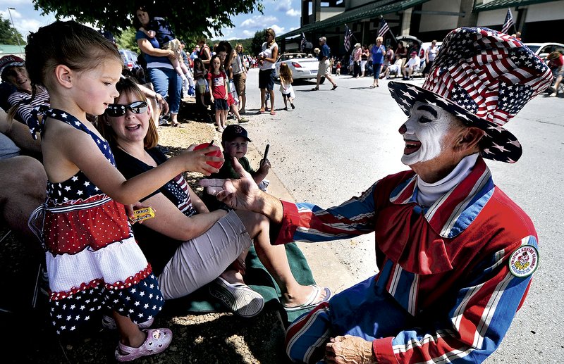 Orren “Bubbles” Moshinski makes a balloon apple for Stella Witt of Bentonville during the Fourth of July parade last year in Bella Vista.