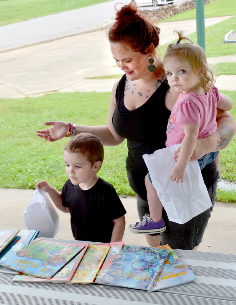 Janelle Jessen/Herald-Leader Melachi Bernard picked out a new book with help from his mom Ashlee Bernard and sister Bethlehem Bernard. The trio were at Bob Henry Park to pick up sack lunches from the Siloam Springs School District&#8217;s Summer Lunch Program. The Allen Elementary School parent-teacher organization also provides a book exchange at the meal pick-up sites.