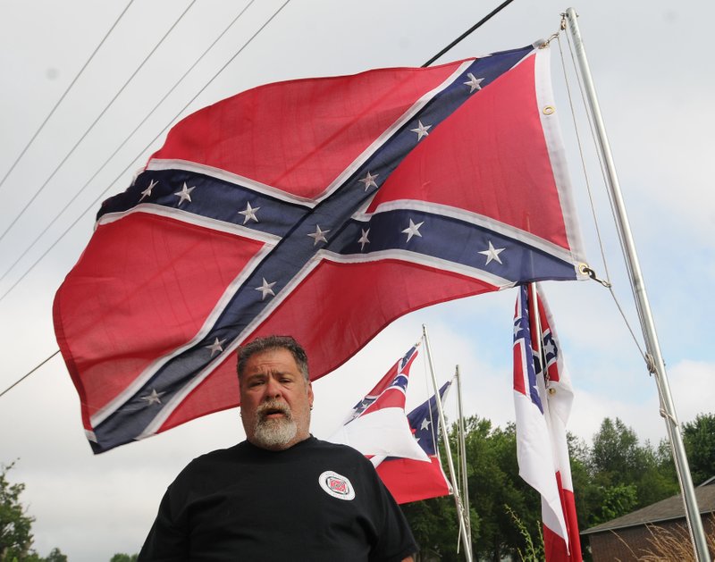 Wayne Fuller flies seven styles of Confederate flags at his home in Rogers. Fuller, standing with the flags Saturday, is proud of the heritage they represent and says the flags honor his ancestors who died in the Civil War.