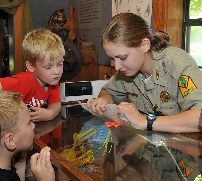 The Sentinel-Record/Mara Kuhn Lake Catherine State Park Interpreter Elizabeth Sorensen, right, reveals art made with beads and an iron as Carson Wakes, 6, left, and his brother Connor Wake, 3, look on at the park on Wednesday.