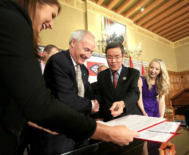 Ashton Campbell (from left) holds out documents for Gov. Asa Hutchinson and Chairman Dinh Thai of Vietnam’s Dong Nai province to sign Monday during a ceremony at the state Capitol. Joining them was Laura Russell.