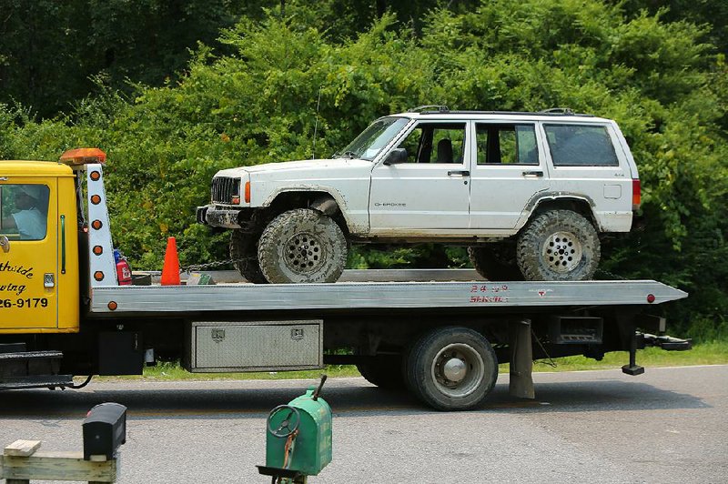 A flatbed tow truck is driven away Tuesday with a Jeep Cherokee that authorities found partially submerged in the Saline River on Tuesday morning with the bodies of a 38-year-old Salem man and his 8-year-old son. Carbon monoxide poisoning is suspected in the deaths, a Saline County sheriff’s office spokesman said. 