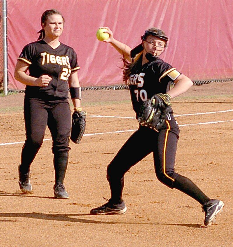 MARK HUMPHREY Prairie Grove pitcher Laney Laymon throws to first base with third baseman Brooke Ketzler backing her up as Laymon fielded a ground ball. Prairie Grove received permisson to play a 4A-1 Conference softball game on Farmington&#8217;s field against Gentry, which the Lady Tigers won 8-4 on April 15.