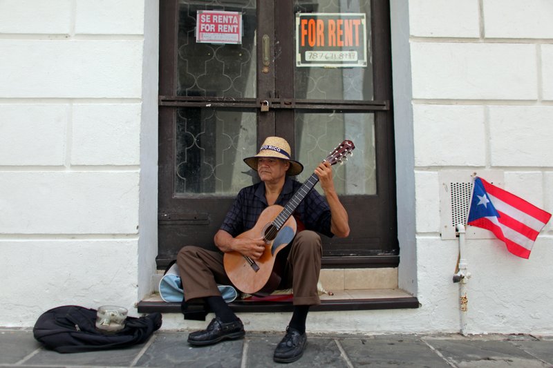 A man plays his guitar while he begs for money in front of a closed down business in Old San Juan, Puerto Rico, Monday, June 29, 2015. International economists released a critical report on Puerto Rico's economy Monday on the heels of the governor's warning that the island can't pay its $72 billion public debt. 