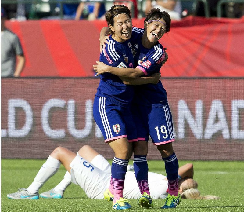 Azus Iwashimizu and Saori Ariyoshi (19) celebrate a berth in the World Cup final against the United States while England’s Steph Houghton lies on the ground Wednesday in Edmonton, Alberta.