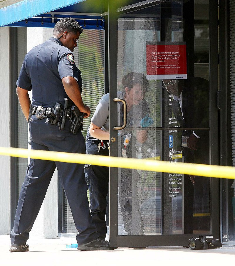A Little Rock police officer assists a crime scene technician dusting for fingerprints on a door at the Bank of America, 4024 West Markham St., after a robbery Wednesday.