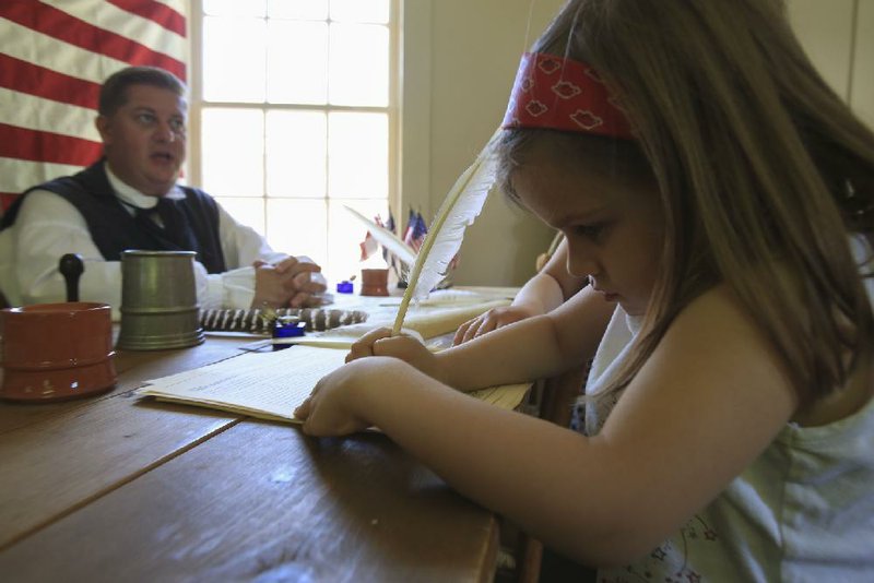 A girl signs a copy of the Declaration of Independence at the Historic Arkansas Museum’s 2014 Frontier Fourth event as Darrell Brown, dressed in period clothing and seated in front of a 1776 flag, provide the document’s history. 