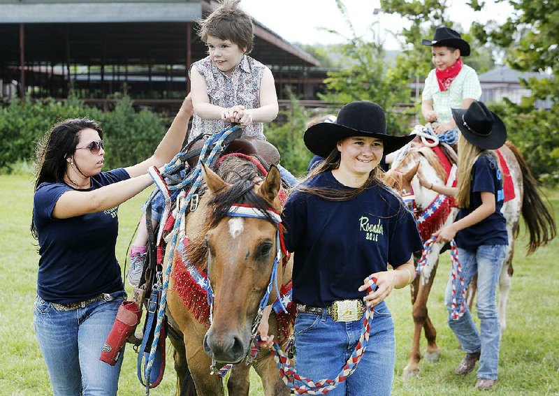 Sydnie Parsons (right) and Lora Husong, both Rodeo of the Ozarks Rounders, walk Claudia Mobbs, 9, on top of Buck, a quarter horse, during Thursday's event.