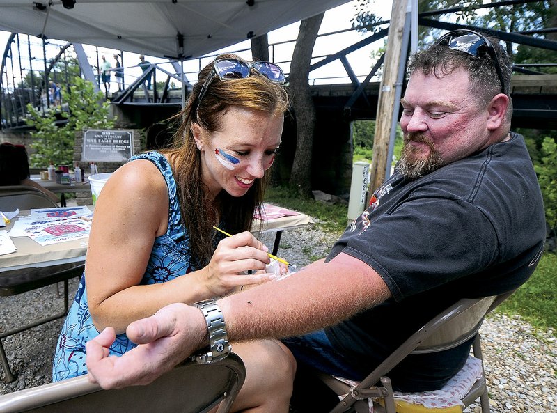 Liz Kapsner, marketing and sales coordinator for War Eagle Mill, paints a U.S. flag on the arm of Troy Morley of Moore, Okla., during last year’s Fourth of July celebration at War Eagle Mill near Rogers.