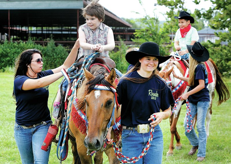 NWA Democrat-Gazette/DAVID GOTTSCHALK Sydnie Parsons (right) and Lora Husong, both Rodeo of the Ozarks Rounders, walk Claudia Mobbs, 9, on top of Buck, a quarter horse, during the event at Parsons Stadium in Springdale.