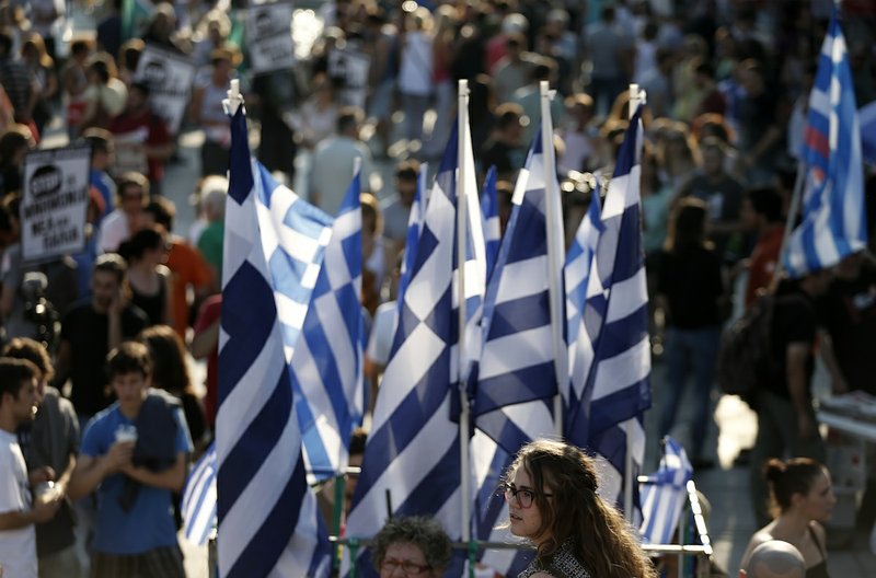 A girl stands in front of Greek flags as people gather before a rally organized by supporters of the No vote at Syntagma square in Athens on Friday, July 3, 2015. Greeks will vote Sunday on whether to accept a proposal that creditors had made of specific reforms in exchange for loans. 