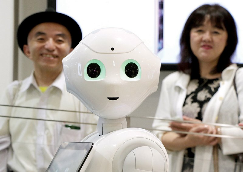 Customers stand in line behind SoftBank Corp.’s humanoid robot Pepper as they wait to pre-order the robot inside the company’s store in Tokyo in June.