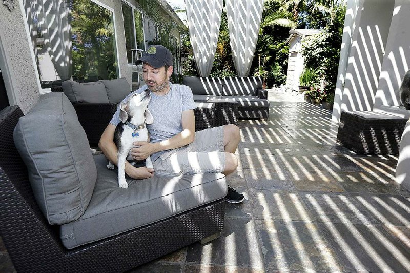 Travis Wills sits with his dog, Sadie, in the backyard of his home in Roseville, Calif., on June 23. Wills, who replaced his front lawn with black mulch and collects water in buckets from his shower and sinks to water the plants in his backyard, said he has not noticed much of a reduction in his water bill.