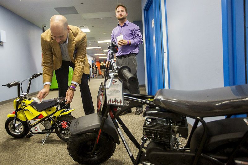 Alex Keechle (left), chief executive officer for Monster Moto, cleans off one of the company’s minibikes Tuesday inside the Wal-Mart home office in Bentonville. 