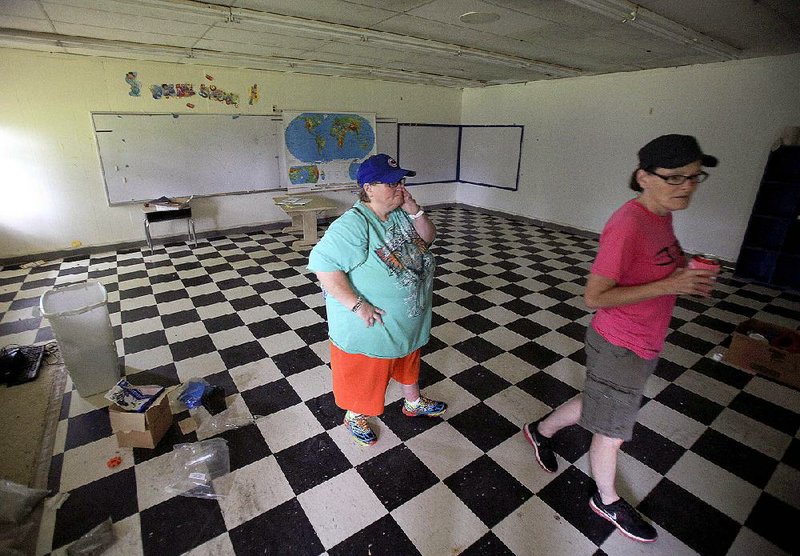 Wilburn High School graduates Shae McMillion (left) and Denise Mann walk through an old classroom at the former school’s campus Wednesday, when it was sold in pieces at auction. The Wilburn School District consolidated with the Concord School District in 2004.
