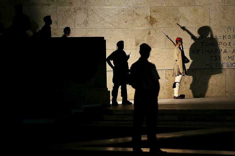 A Greek presidential guard watches over the Tomb of the Unknown Soldier as riot police guard one of the entrances to Parliament during a Sunday demonstration in Athens, Greece, by supporters of the no vote on last week’s referendum on austerity measures.