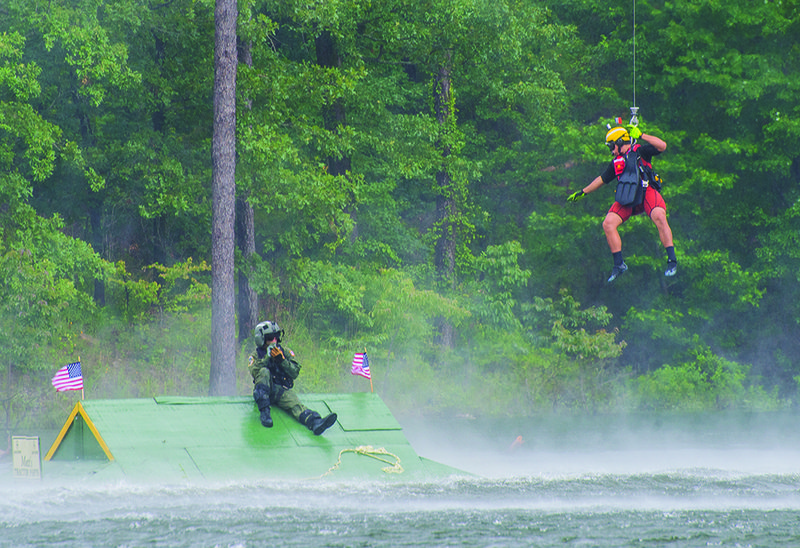 A rescuer hangs from the Coast Guard helicopter as he reaches out for the "victim" that sits atop a rooftop during the 12th annual Arkansas Fire Boat School.