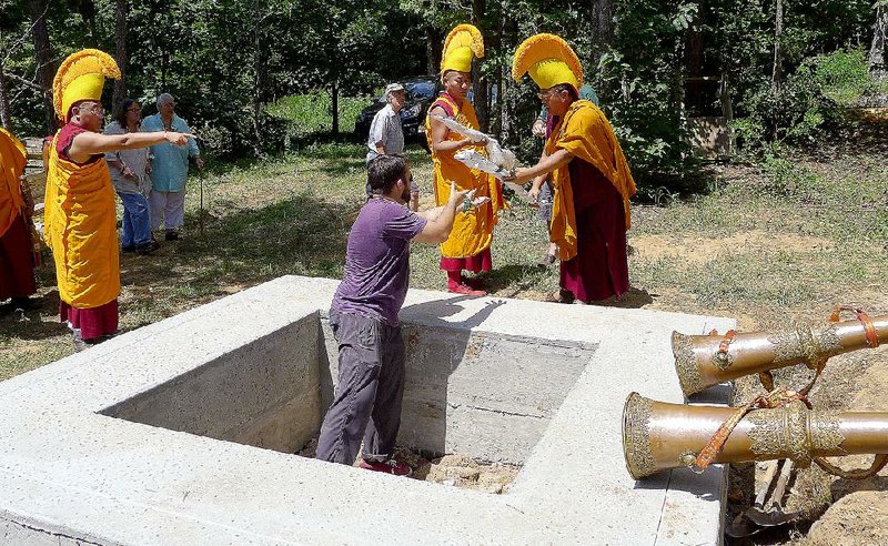 Geshe Dakpa Jigme of India (left) and Geshe Thupten Dorjee, who lives in Fayetteville, hand rifles to Wesley Clawson to bury in the foundation of a Tibetan Buddhist monument being constructed in rural Madison County near Crosses. Clawson is president of the Tibetan Cultural Institute of Arkansas.