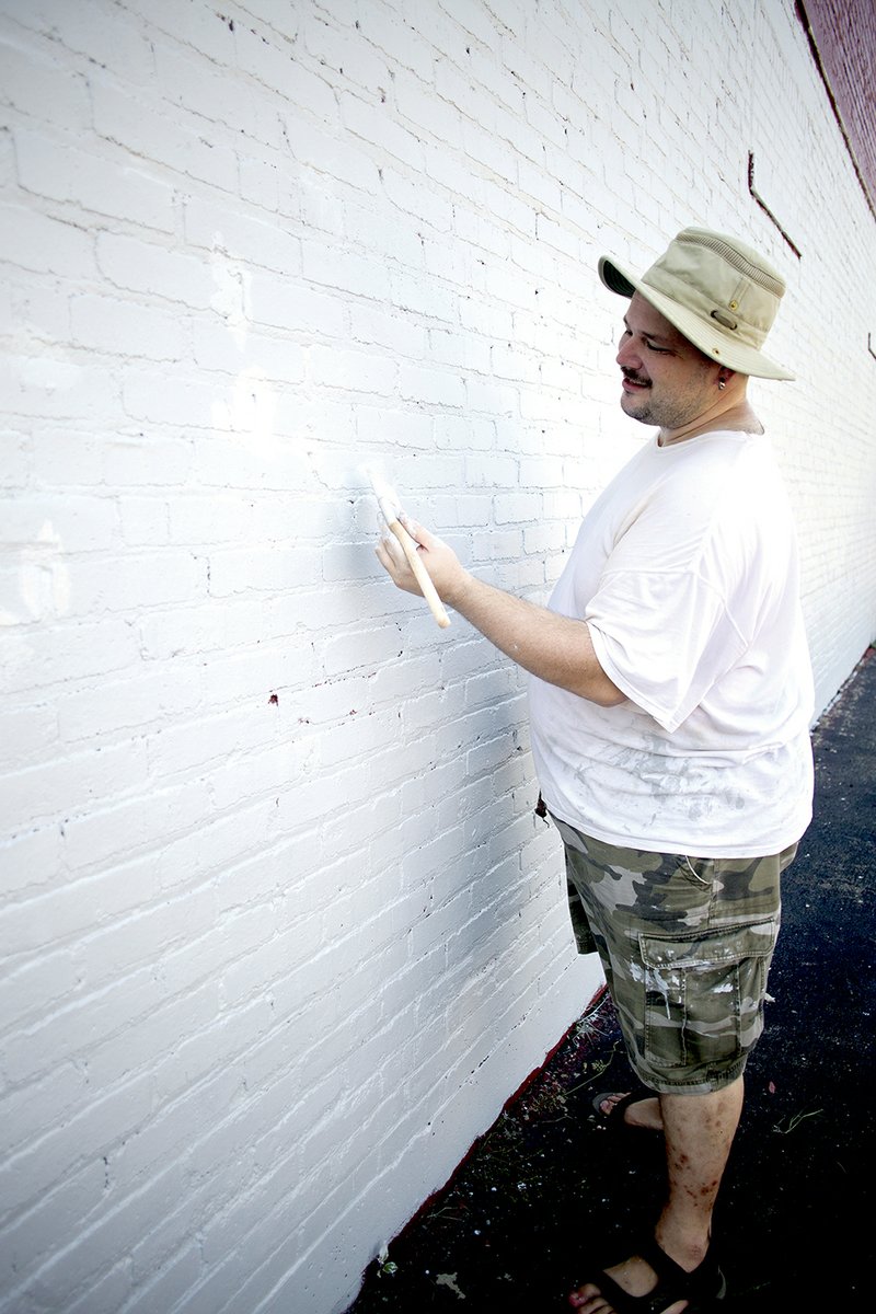 Thomas Fernandez, an art instructor at Arkansas State University-Beebe, paints a white coat on a wall of the Wilbur D. Mills Educational Services Cooperative building as the first step in painting a veterans mural.