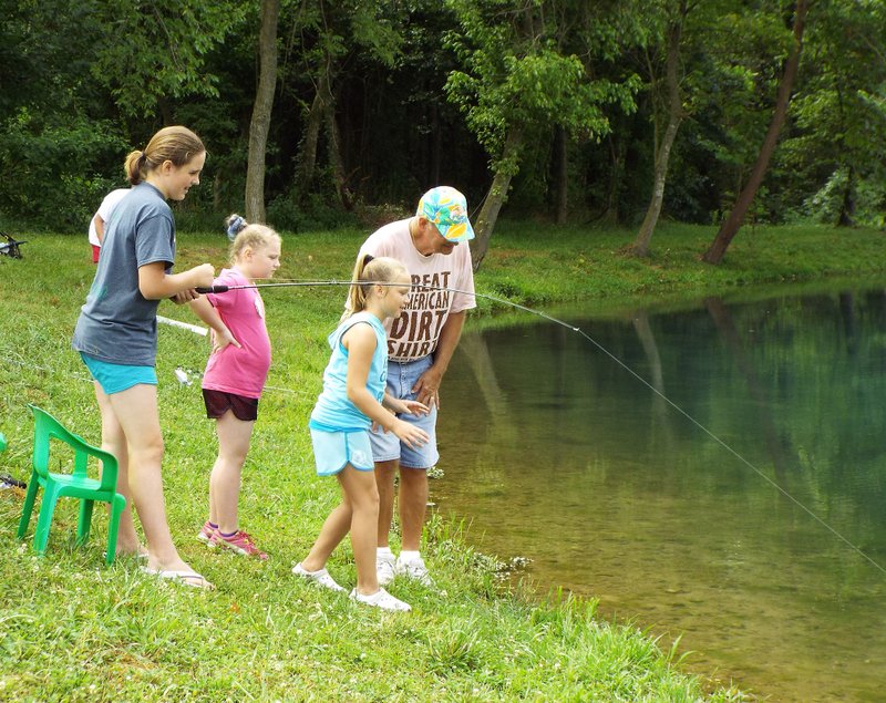 Assisted by Ray Arnold (right), youngsters who attended the "Kids in the Woods" event on July 20 and 21 had opportunity to try out their fishing skills in the ponds at the Flint Creek Nature Area in Gentry. Emily Jessen had a catfish on the line and was bringing it in.