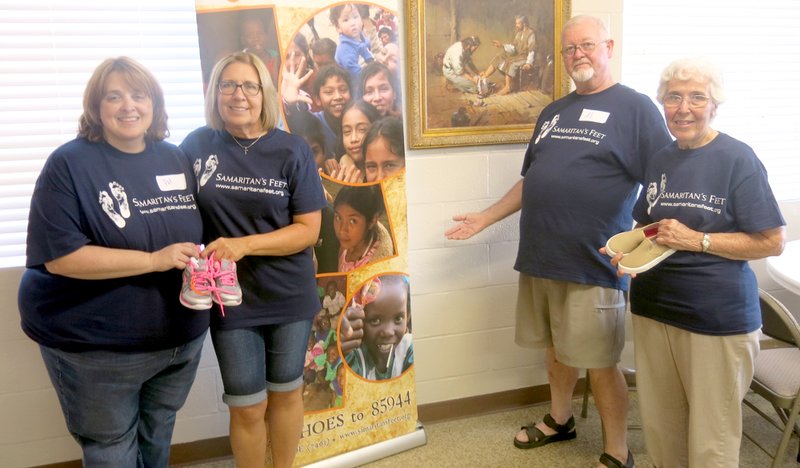 Photo by Susan Holland Pat Bodenhamer, left, pastor of the Gravette United Methodist Church, poses with Lori Pinkerton, Al Blair and Jo Phillips, as they show some of the shoes given away at the Samaritan&#8217;s Feet event Saturday evening at the church. Al points out the poster showing children throughout the world who have been helped by the annual shoe distribution.