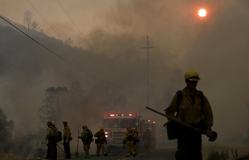 Firefighters walk under smoke from fires along Morgan Valley Road near Lower Lake, Calif., Friday, July 31, 2015. A series of wildfires were intensified by dry vegetation, triple-digit temperatures and gusting winds.