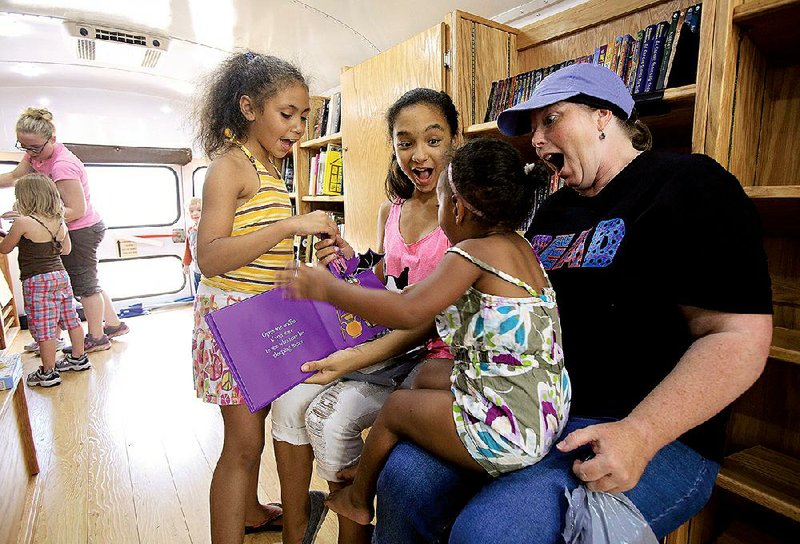 Librarian Kay Calvert (right) reads a book with Tai Yah Tims (from left), Zoe McGee and Ta’Miyah Tims during the Beebe Badger Bookmobile’s stop Wednesday at Edward Lunnie Memorial Park in Beebe. 