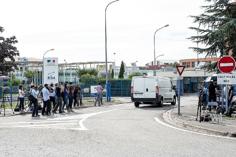 Journalists watch as a white van, transporting debris that washed up on an Indian Ocean island and is believed to be part of a Boeing 777, arrives at a military testing facility in Balma, France. 