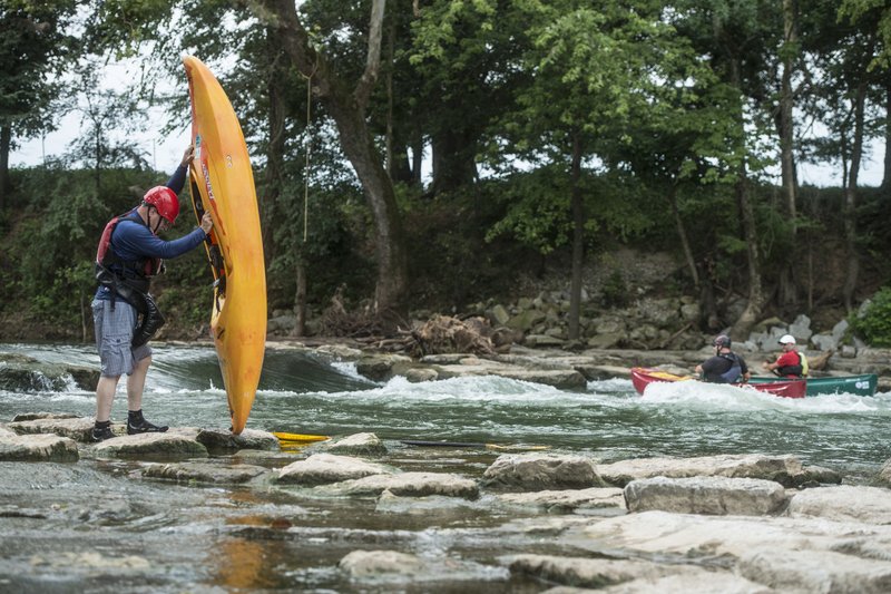 Larry Tucker of Bella Vista drains the water from his kayak Friday at the Siloam Springs Kayak Park just south of Siloam Springs. Tucker has been kayaking for a few years and regularly uses the kayak park since it opened. Many smaller communities like Siloam Springs improve the amenities they offer, like adding splash parks, bike trail and disc golf courses to compete with other cities.