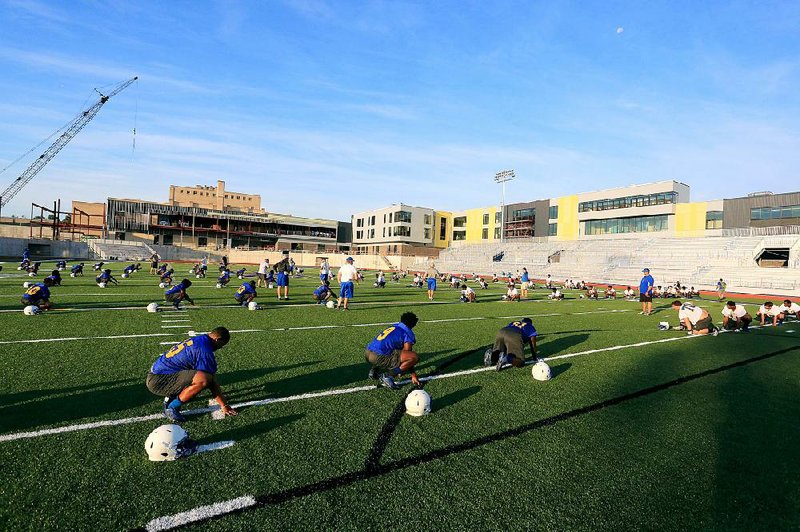 North Little Rock players go through stretching exercises during the first day of fall practice Monday at their new on-campus stadium. The Charging Wildcats, with new coach Jamie Mitchell taking over for the fired Brad Bolding, were forced to practice during the preseason last year on softball fields at Burns Park because the stadium was still under construction. But with the facility nearing completion, the team was able to work out in shorts and helmets on their new field.