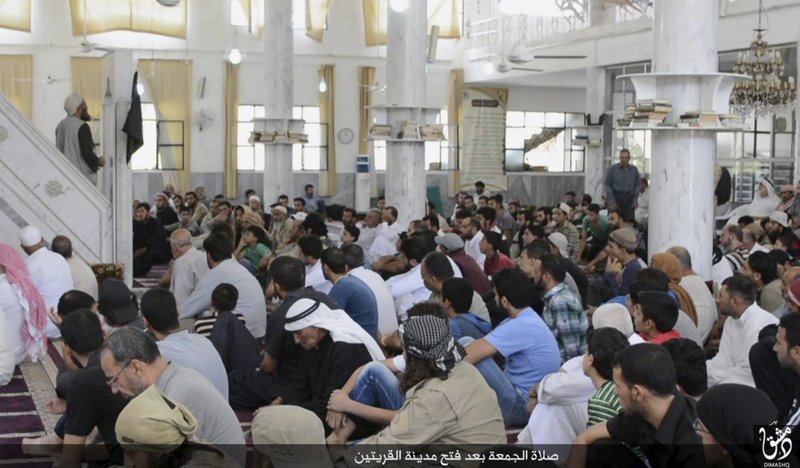 In this photo provided Friday, Aug. 7, 2015, by the Rased News Network, a Facebook page affiliated with Islamic State militants, Muslim worshipers attend Friday prayers in a mosque in the central Syrian town of Qaryatain. The Arabic on the bottom banner reads, "Friday prayers after the conquest of Qaryatain." Activists on Saturday said hundreds of families fled the Christian town of Sadad as Islamic State militants captured Qaryatain on Thursday, which is about 25 kilometers (15 miles) northwest of Sadad.