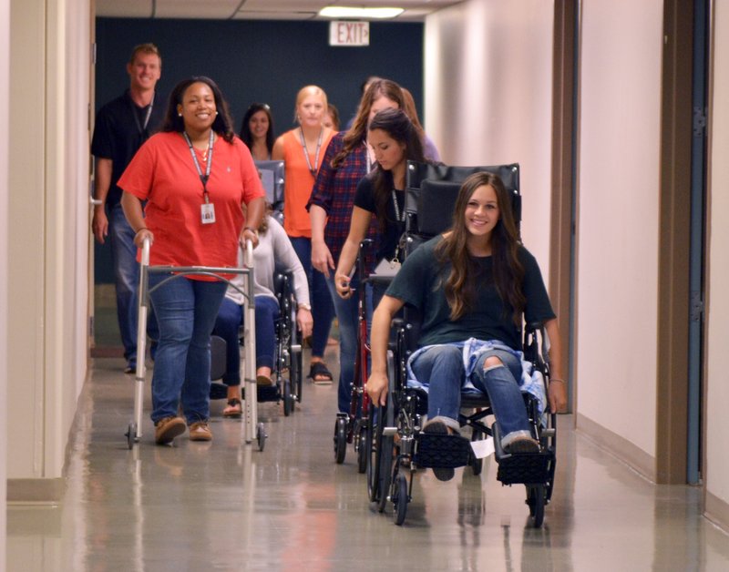 Megan Campbell (right), a new physical therapy doctoral student, pushes herself in a wheelchair Friday as other students follow while touring the University of Arkansas for Medical Sciences building in Fayetteville. The students took the tour in the same way their disabled patients might tour the building. For photo galleries, go to nwadg.com/photos.